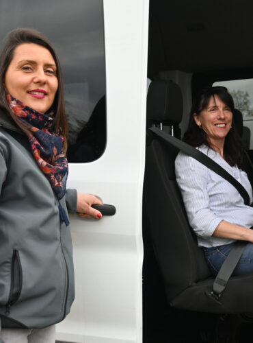Conductrice Transphere ouvrant la portière d’un minibus pour une passagère lors d’un ramassage d’usine